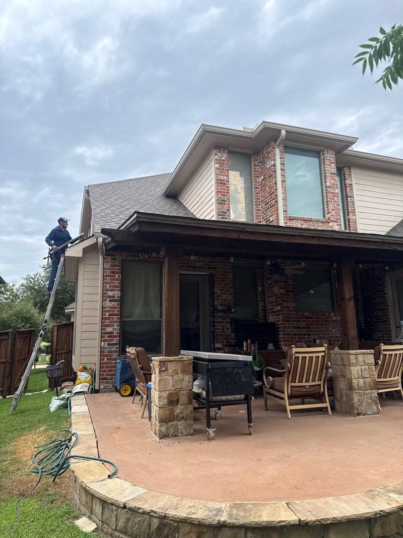 Crew member on a ladder working on the gutter line at the eave of a two-story brick and siding home