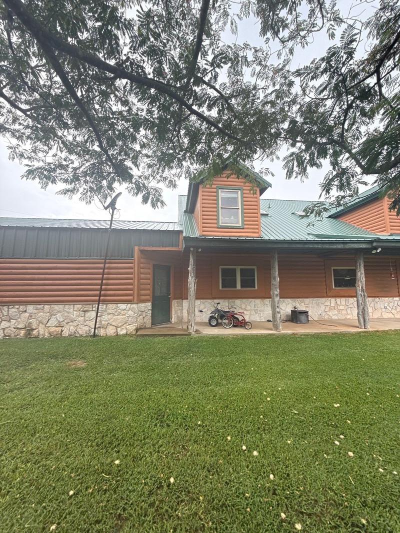 Green standing seam metal roof on a log-look siding home with a stone base and covered porch