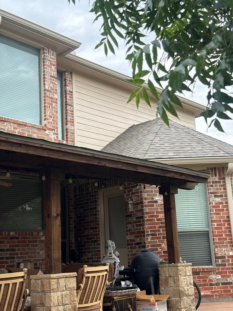 Stained-wood covered patio with cedar posts on stone column bases, attached to a two-story brick home