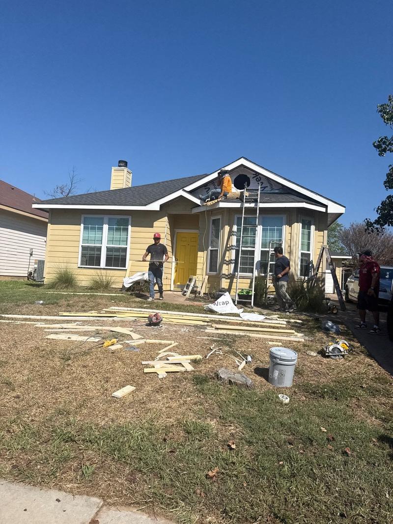 Siding crew working from ladders and the porch roof while replacing lap siding on a yellow house