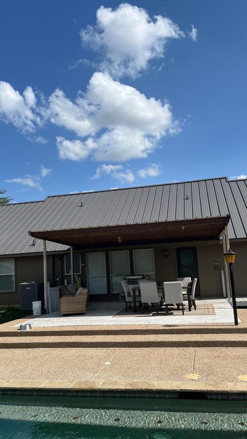 Standing seam metal roof seen across a backyard pool on a brick ranch home