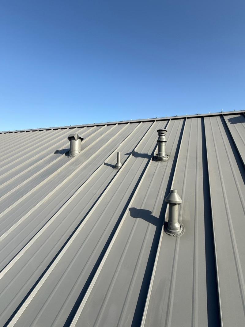 Close-up of a gray standing seam metal roof with matching painted vent stacks and pipe flashings