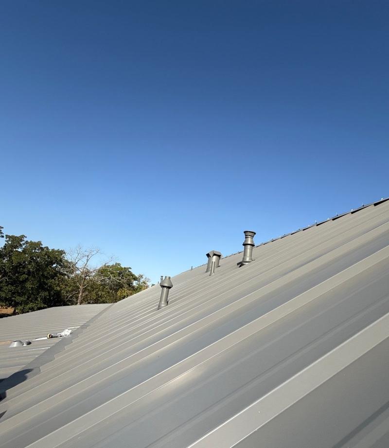 Gray standing seam metal roof panels running up to the ridge, with painted vent stacks