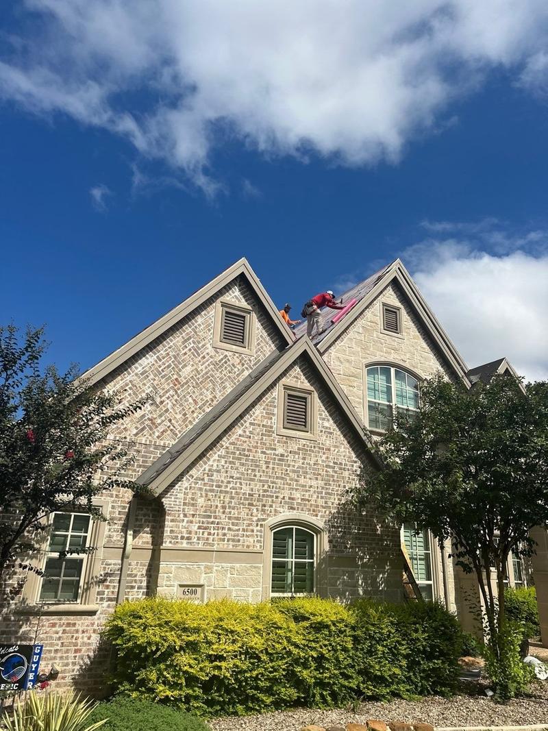 Roofers installing shingles on a steep gable of a two-story stone and brick home